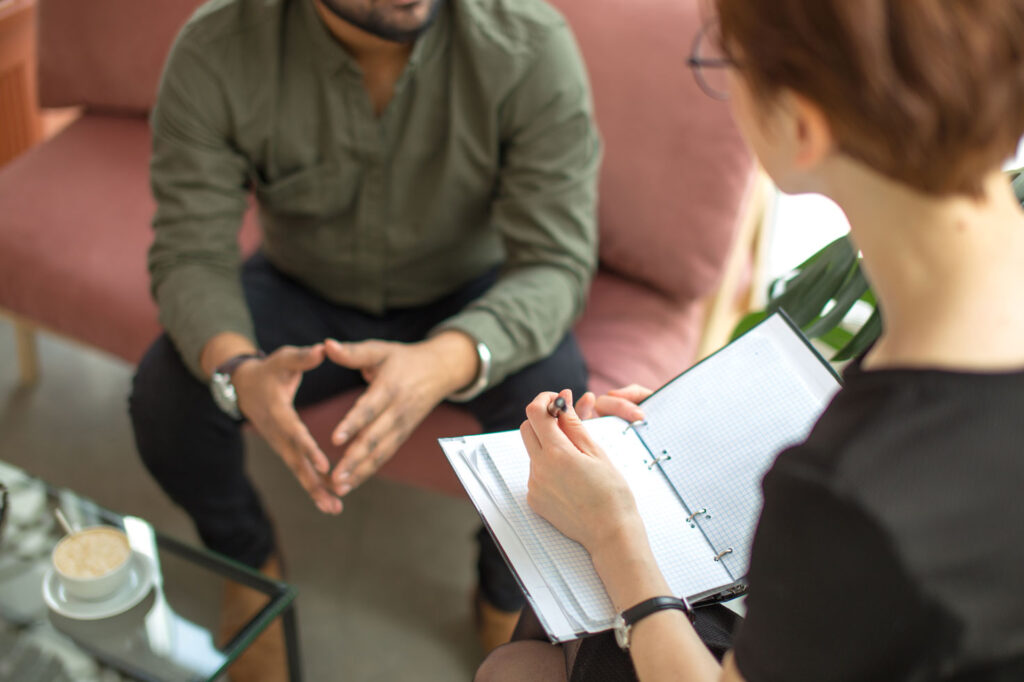 woman holding notebook as a person on a couch sits opposite with hands folded